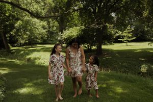 Children wearing coordinated floral outfits play together on green grass under trees.