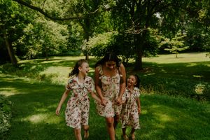 Three people in coordinated floral outfits walk through a sunny park setting.