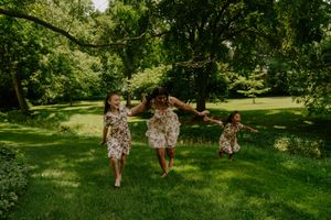 Three figures in matching floral outfits run and play together in a lush park setting.