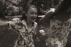 A black and white photo captures joyful movement in a park setting with matching floral dresses.