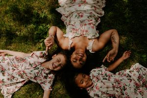 Overhead view of three people in floral dresses lying on grass in a circular formation.