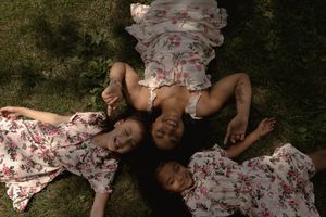 Three people in matching floral outfits lay in grass forming a circle while laughing.