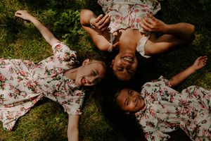 Overhead shot of three people in floral dresses laughing while lying in grass.