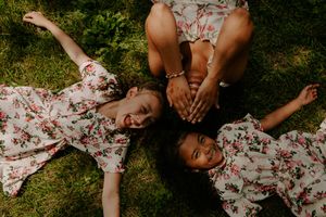 Three people in matching floral dresses lay in grass making silly expressions.