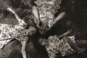 Black and white portrait of children lying on grass with floral dresses.