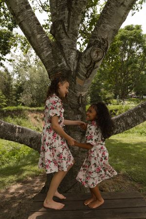Children in matching floral outfits play around a large tree trunk on a wooden platform.