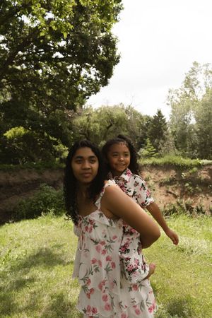 Two people wearing matching floral dresses stand in a sunlit meadow.