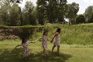 People in floral dresses walking through tall grass in a sunny field.