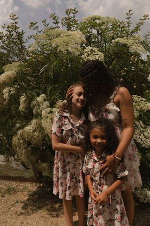 Two people in matching floral dresses explore flowering bushes in a meadow.