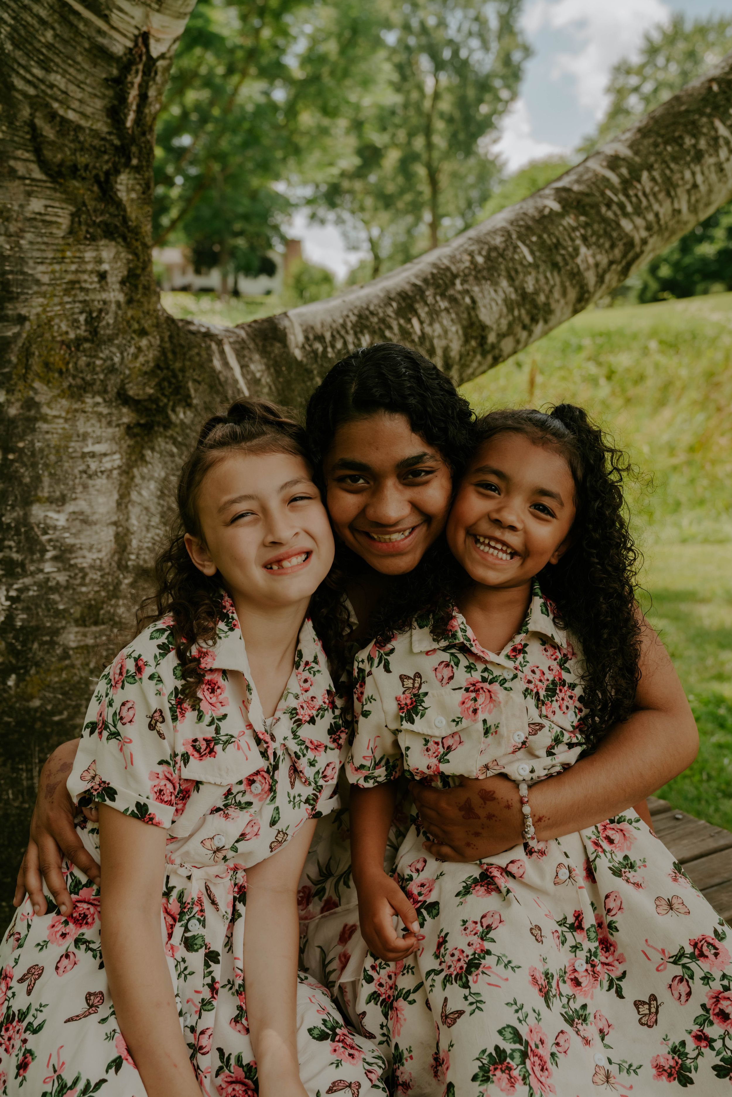Joyful outdoor portraits featuring matching floral dresses against a natural backdrop.