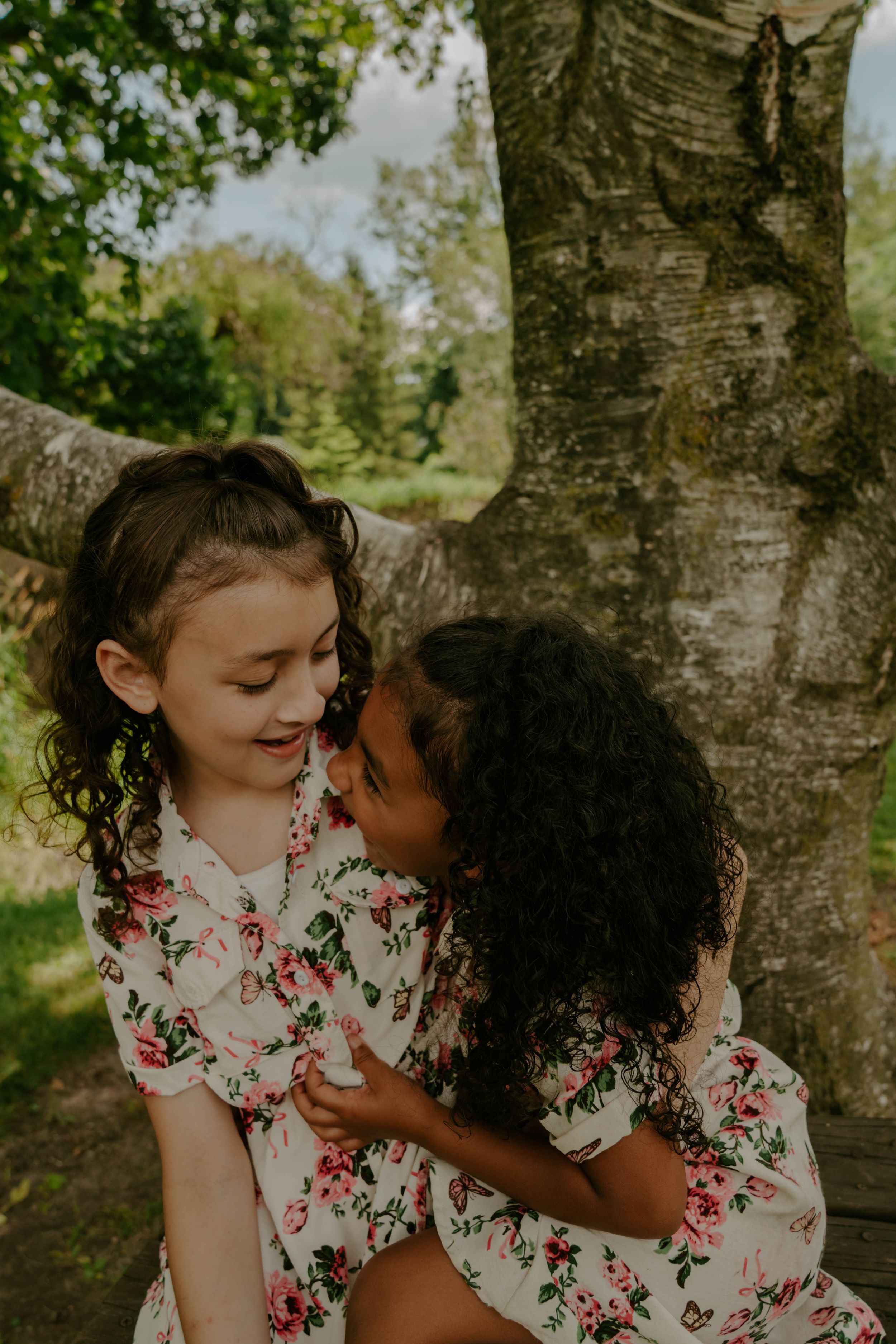 Sweet candid moments captured of children in floral prints playing near a rustic tree.