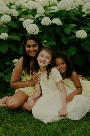 Candid portrait of children laying in grass beside flowering hydrangea bushes.