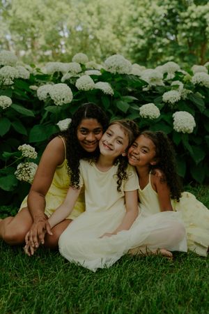 Playful summer portrait of children in cream dresses lounging by flowering bushes.