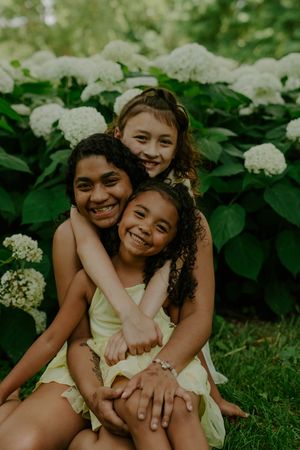 Natural candid moments of children playing and embracing on grass near flowering bushes.
