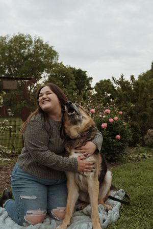 German Shepherd mix dog cuddling on blanket in garden with pink roses in background.