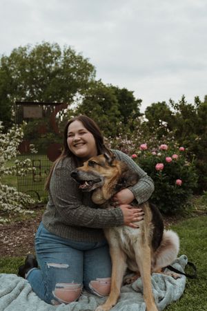 Playful dog interaction on blue blanket with flowering bushes in background.