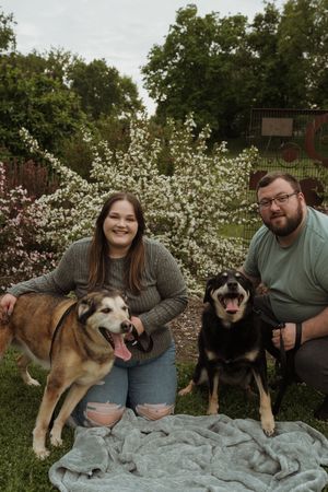 Family portrait with two dogs sitting on blue blanket in garden setting.