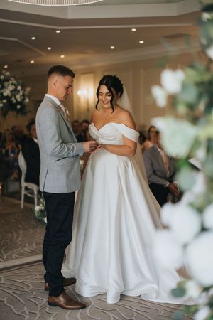 A couple exchanges rings during an elegant indoor wedding ceremony with white floral decorations.