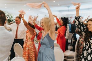 Celebration on a dance floor at a wedding reception with guests dancing and waving napkins in the air.