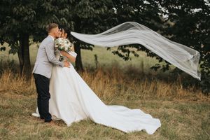 A couple embraces in a field as a long white veil flows dramatically in the wind.