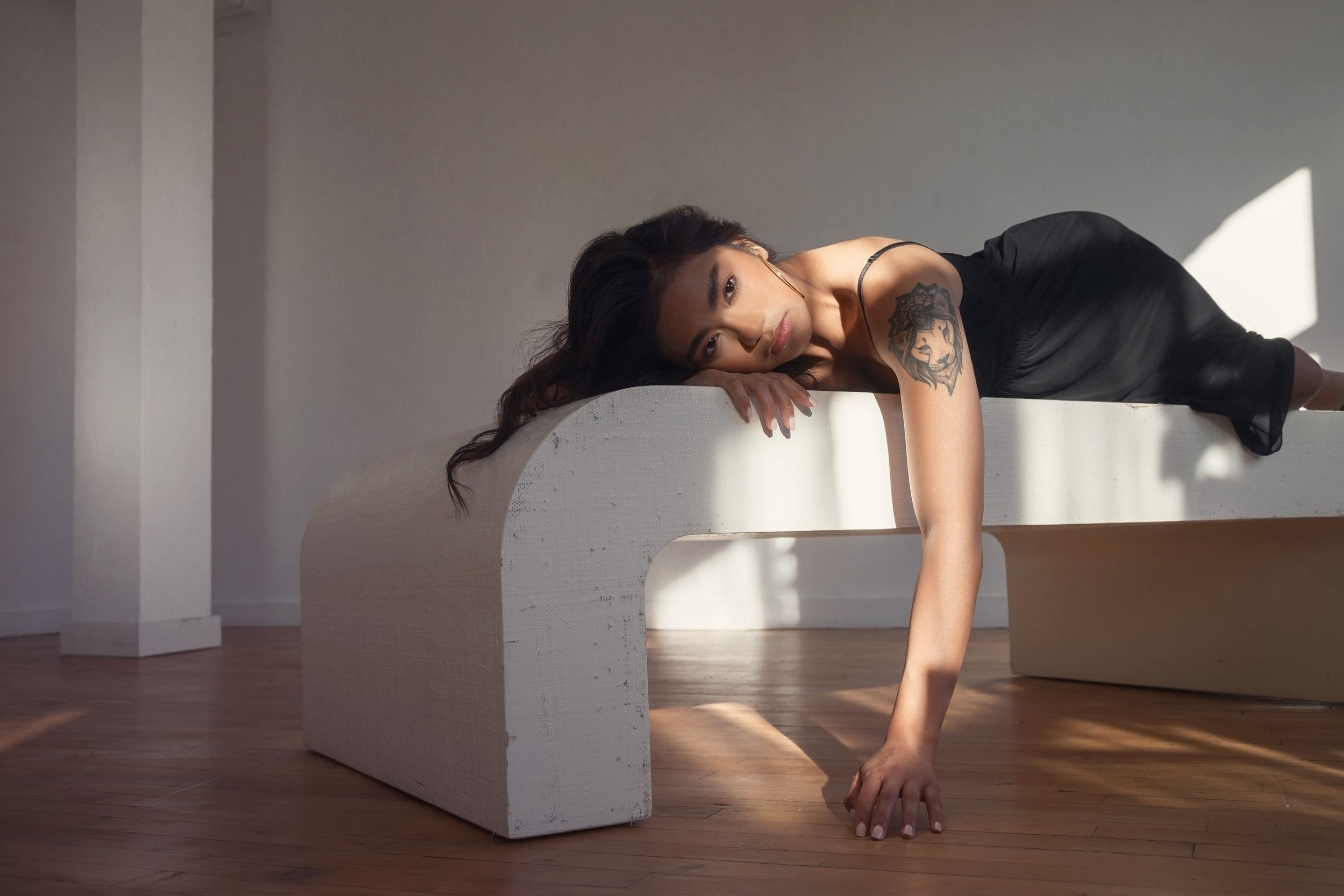 Athletic figure in black workout attire performing a plank pose on a white geometric block in sunlit studio space.