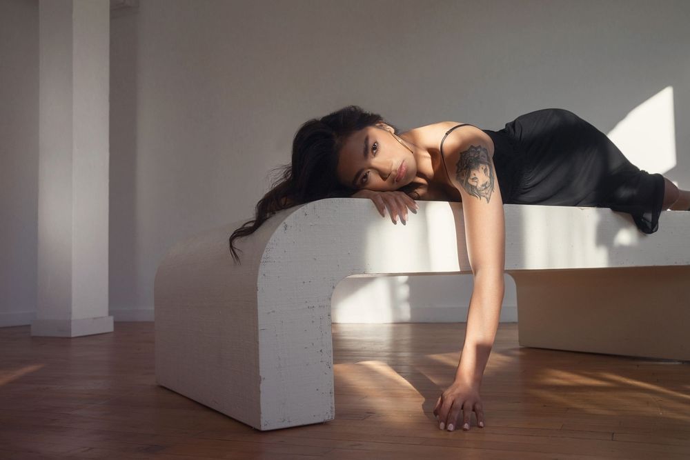 Athletic figure in black workout attire performing a plank pose on a white geometric block in sunlit studio space.
