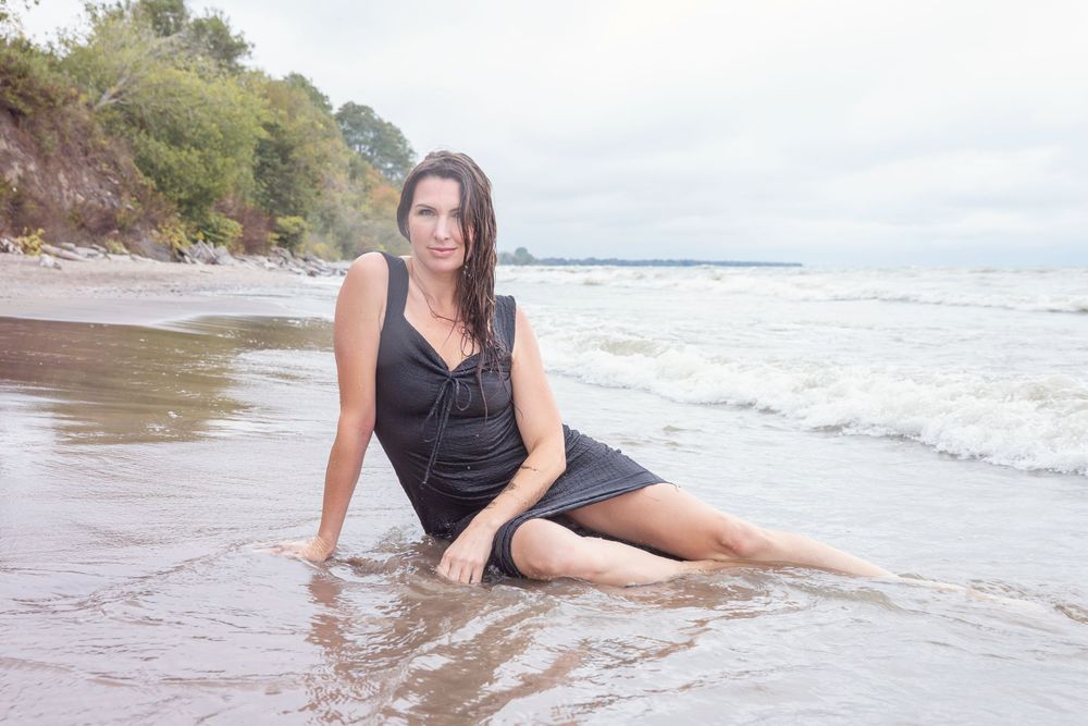 Person in black beach attire relaxes on sandy shoreline as waves roll in during a summer day at the beach.