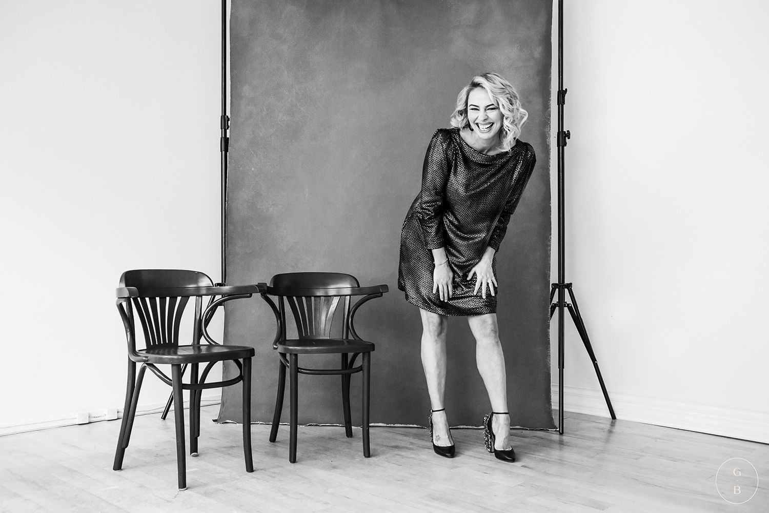Black and white portrait with wooden chairs against white wall in minimalist studio setting.