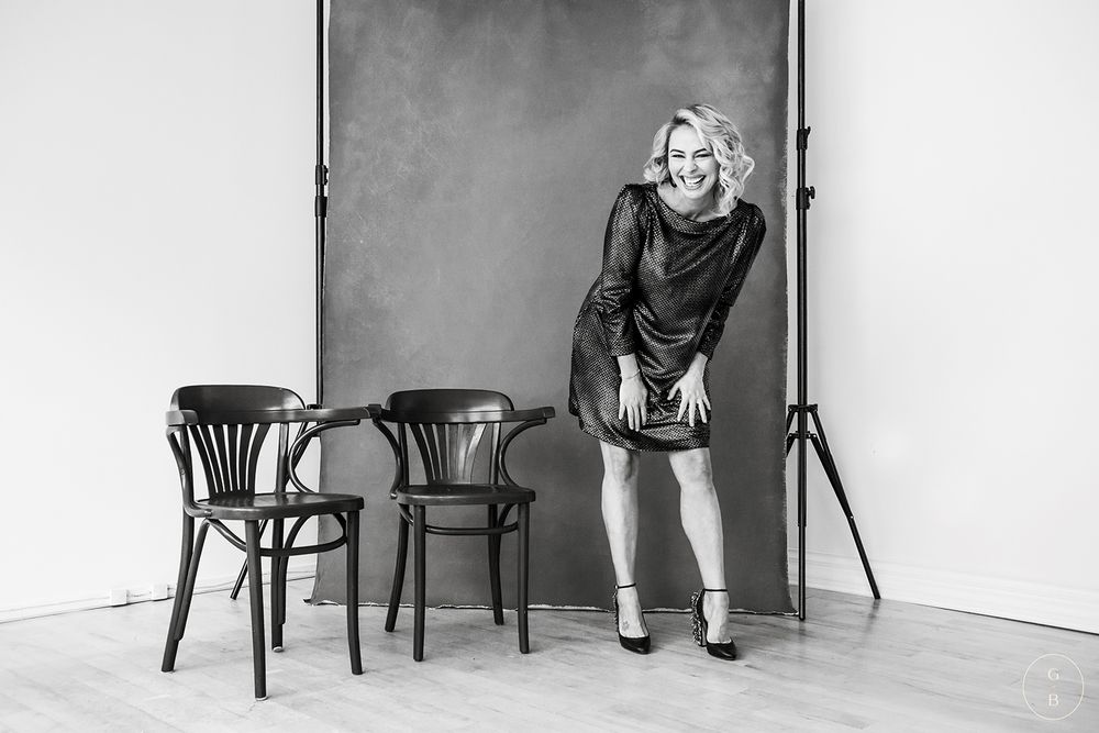Black and white portrait with wooden chairs against white wall in minimalist studio setting.