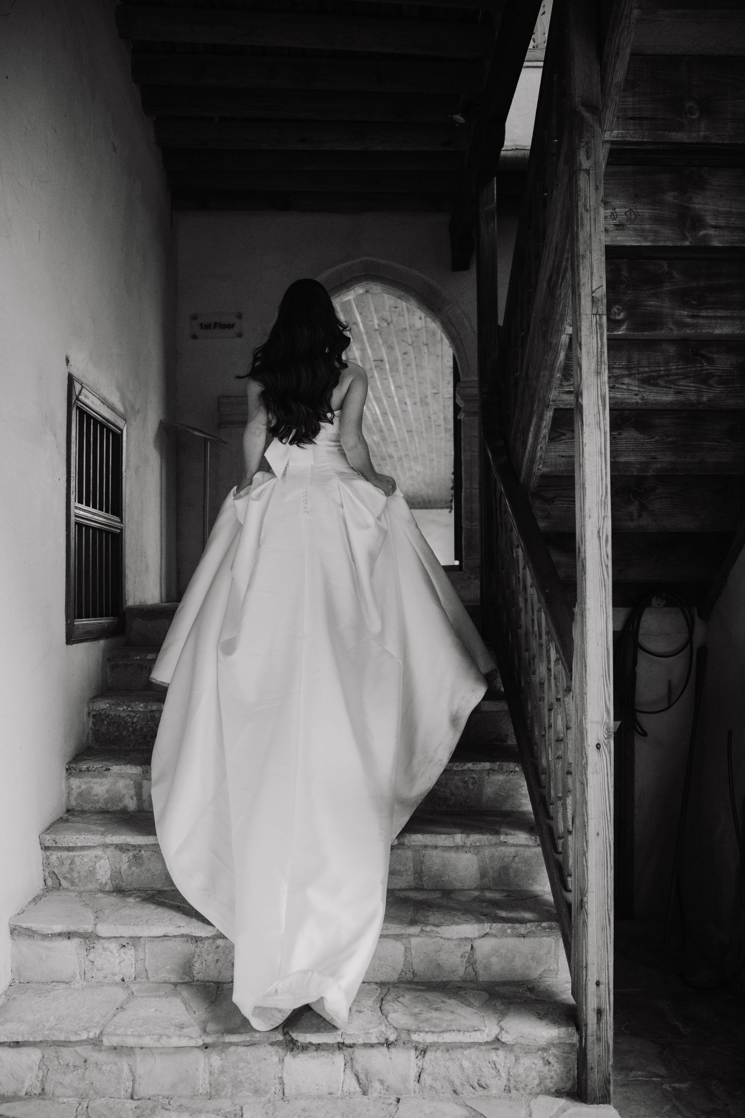 A flowing white wedding gown with intricate lace details photographed against ancient stone arches.
