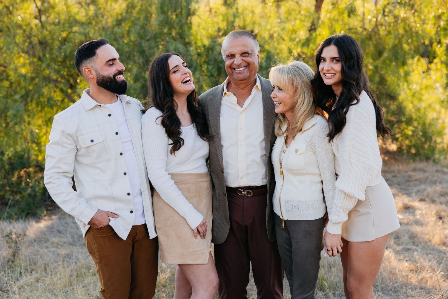 Five people laughing together outdoors during a golden hour family photo session in a natural setting.