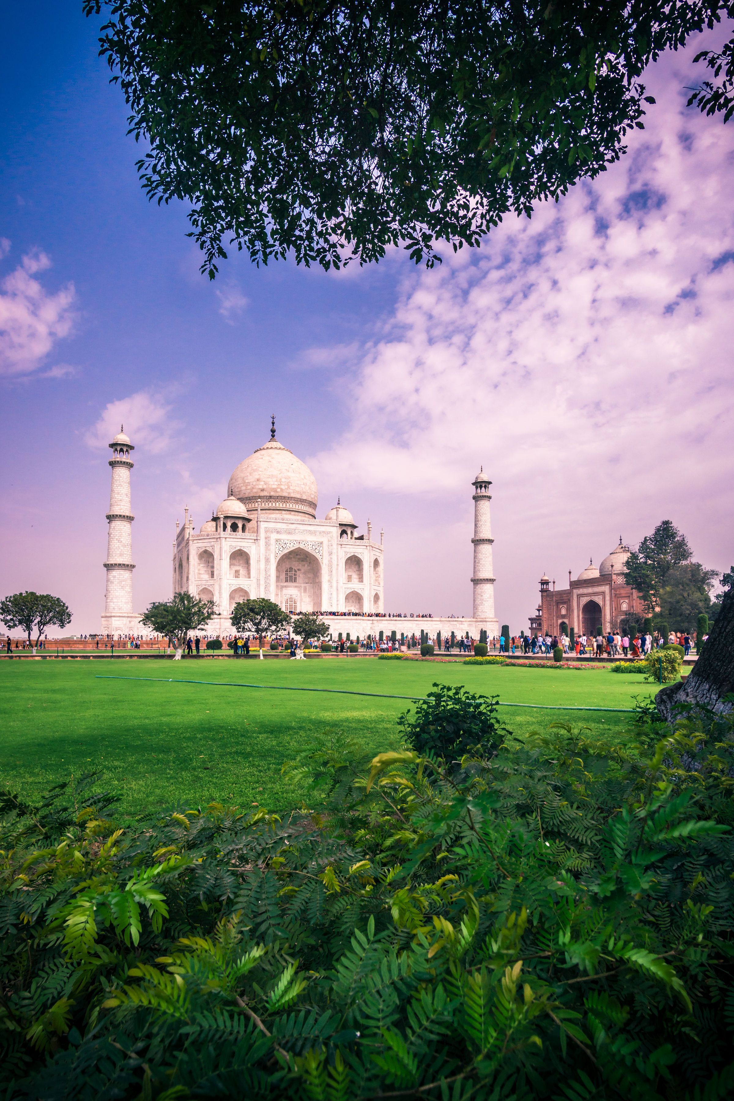 Panoramic view of the Taj Mahal with lush green gardens and monsoon clouds in Agra, India during summer.