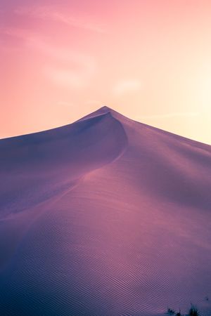 Stunning desert sand dunes against a pink and purple sunset sky creating a dreamy ethereal landscape at dusk.