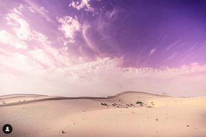 Pink and purple clouds fill a dramatic sunset sky over silhouetted hills in a panoramic landscape view.