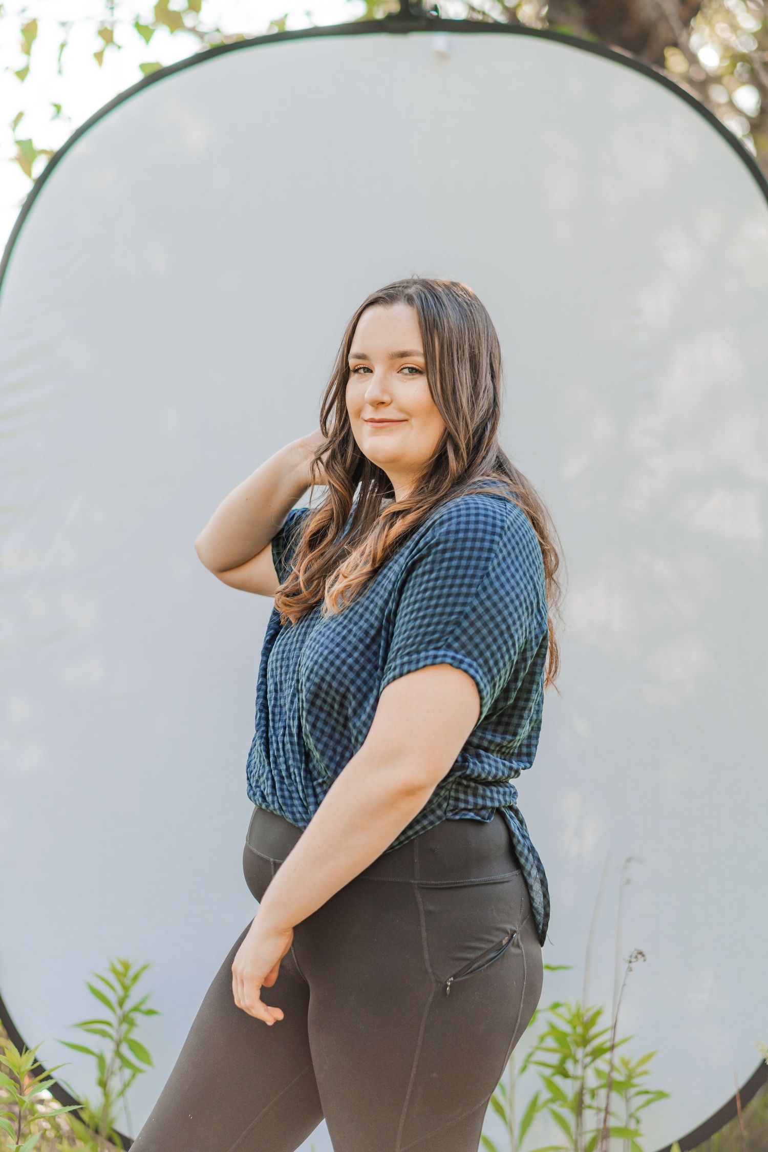 Woman poses confidently in front of a pop-up backdrop in nature, surrounded by greenery and soft sunlight in the Pacific Northwest.