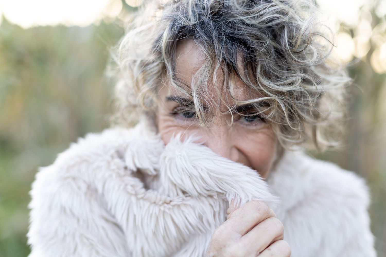 Portrait of a curly-haired woman partially covering her face with her soft jacket.