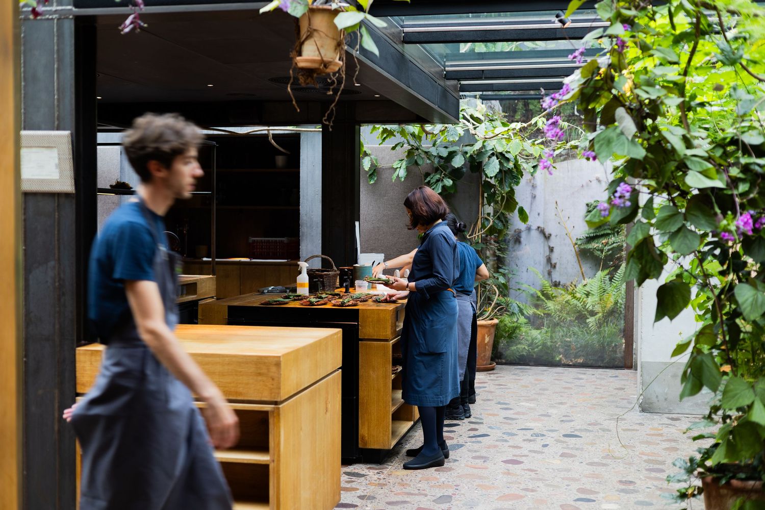 Restaurant kitchen counter with staff working in a garden-lined courtyard setting.