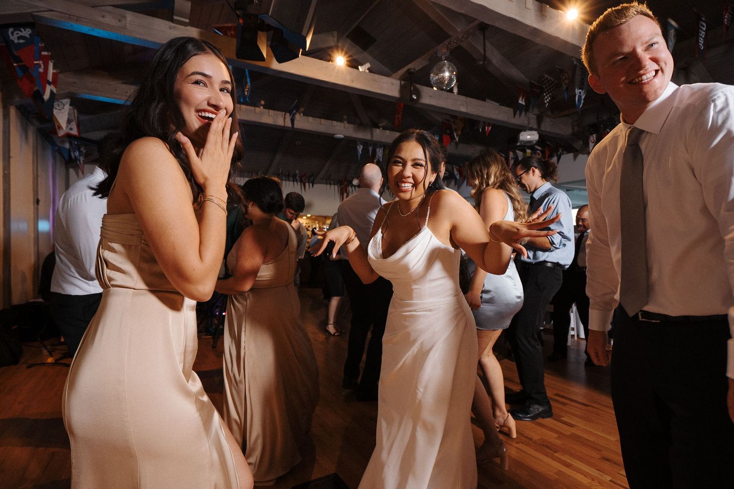 Wedding guests dressed in white dance and celebrate with joyful expressions at an indoor reception venue.