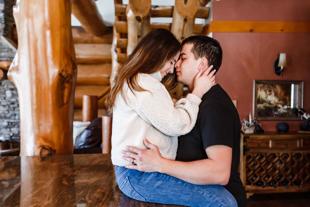 A couple sharing a romantic kiss while sitting in a cozy log cabin interior with wooden beams.