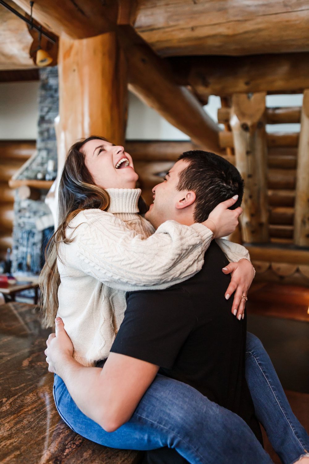 Couple sharing joyful laughter while sitting in a cozy rustic cabin with wooden beam interior.
