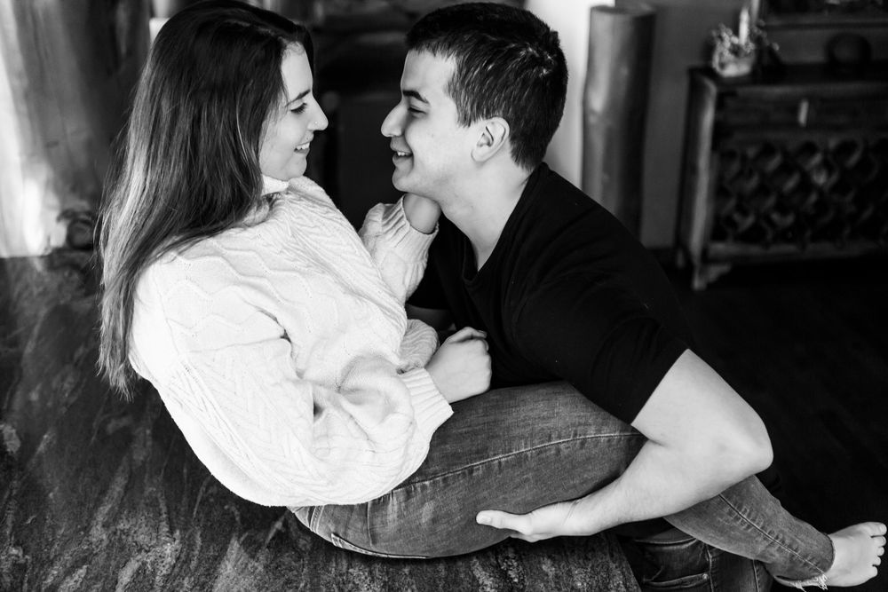 A couple in black and white share an intimate moment while sitting on a wooden floor.