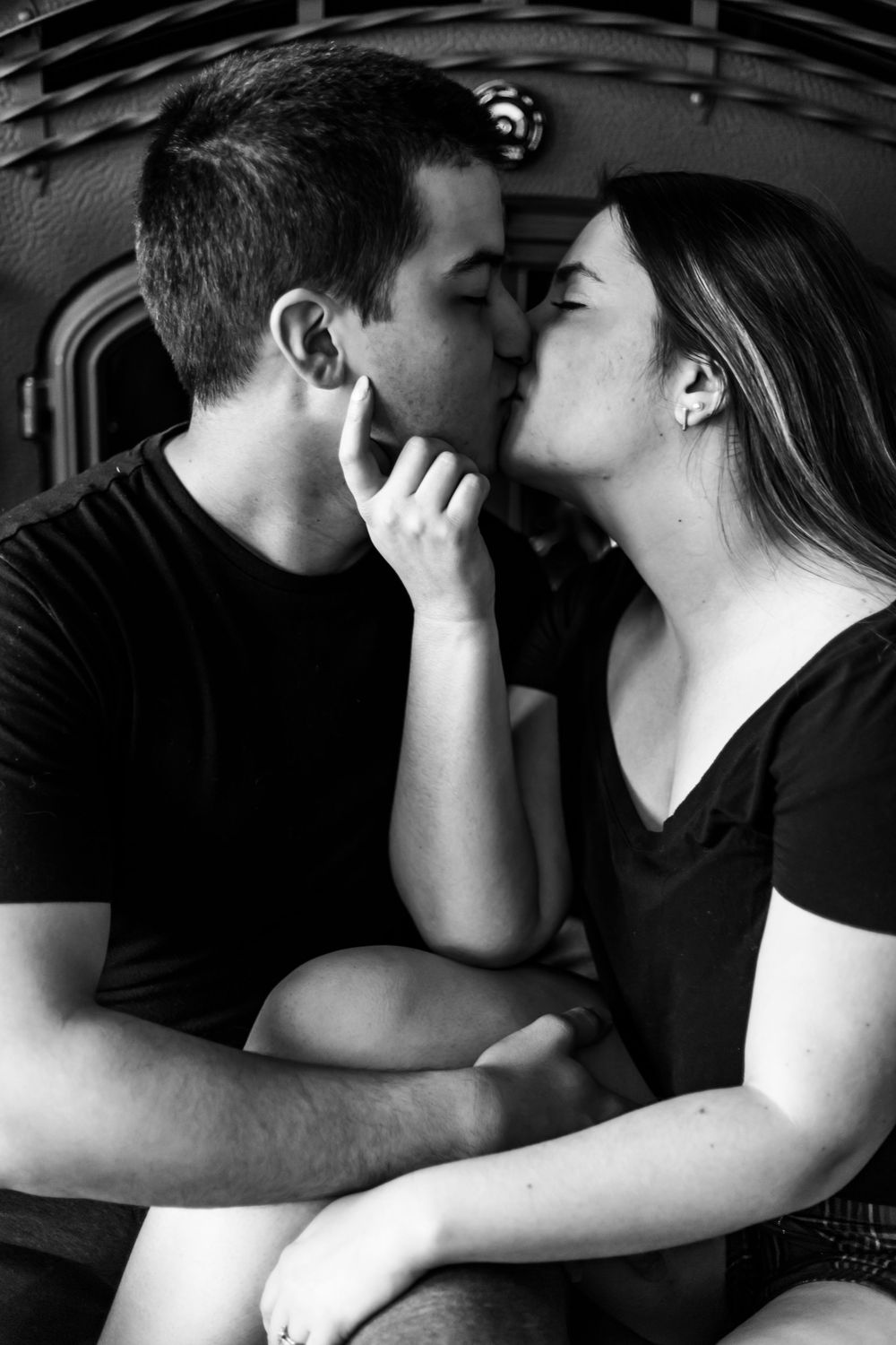 Black and white romantic photograph of a tender moment between a couple sharing a kiss, both wearing dark t-shirts.