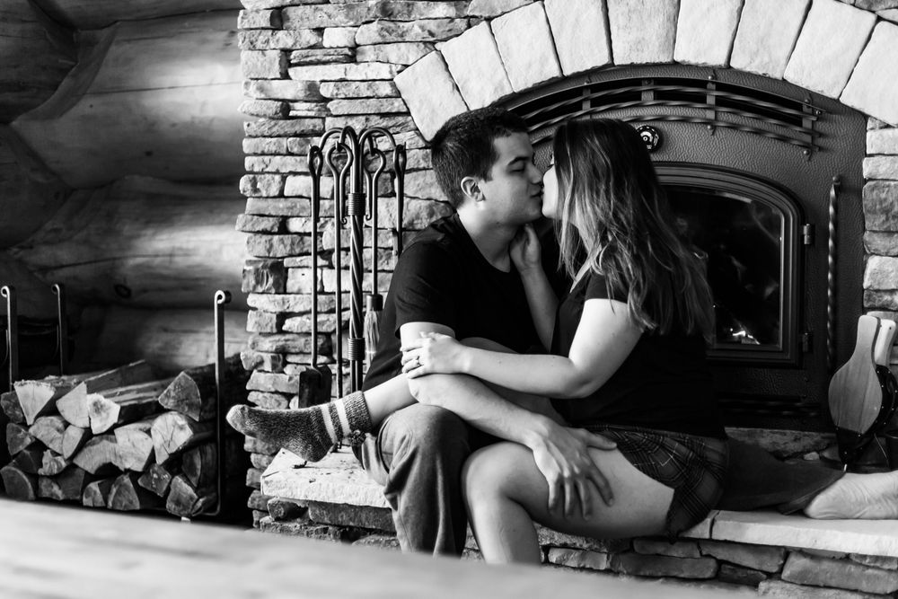 A romantic black and white photo of a couple embracing near a rustic stone fireplace.