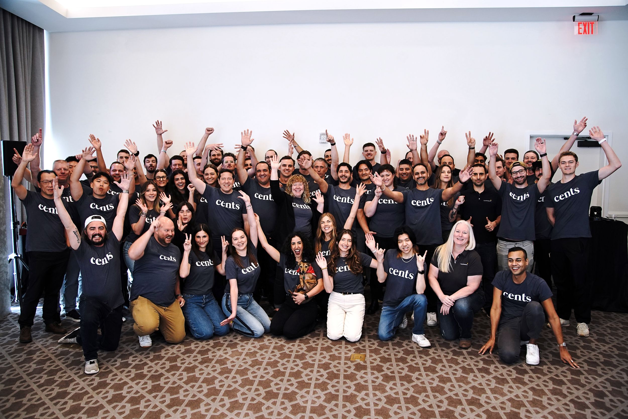 Large group of employees posing together for a company photo with raised arms.