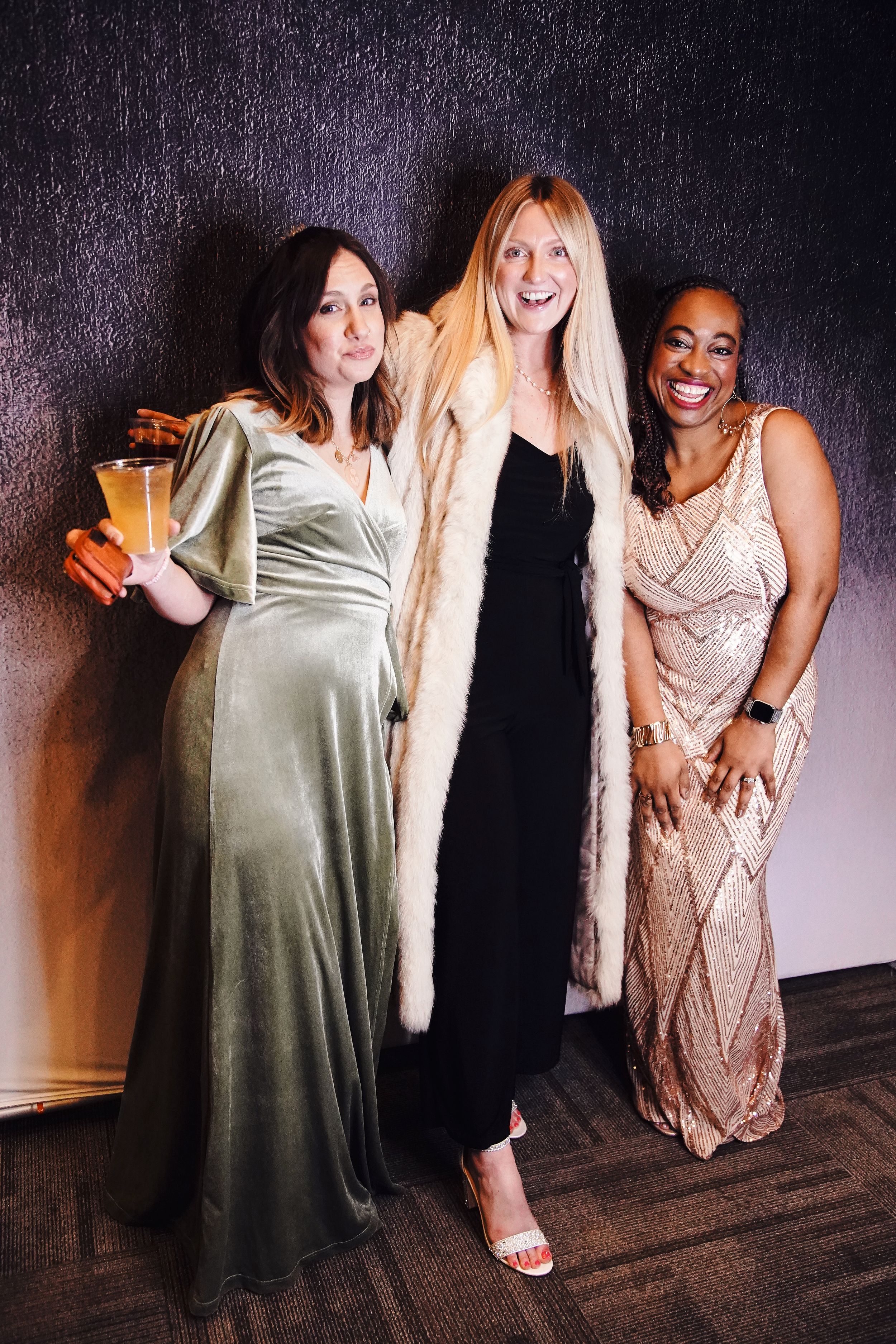 Group of friends in formal dresses posing and laughing at a party.