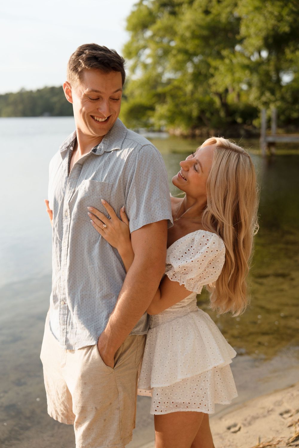 Joyful couple laughing together on lakeside beach during golden hour photoshoot.