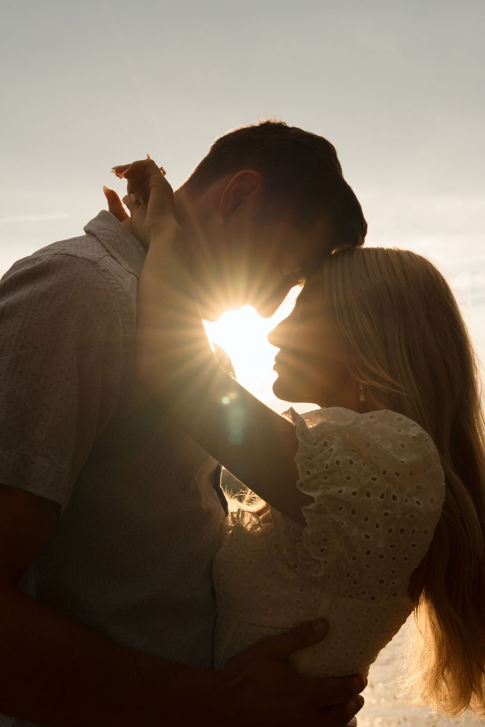 Silhouetted couple sharing an intimate moment at sunset with sun rays creating a dreamy backlit effect.