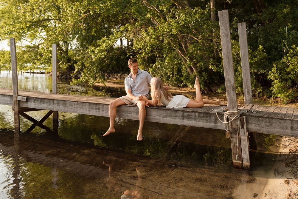 A couple sitting together on a wooden dock by the lake on a sunny summer day.