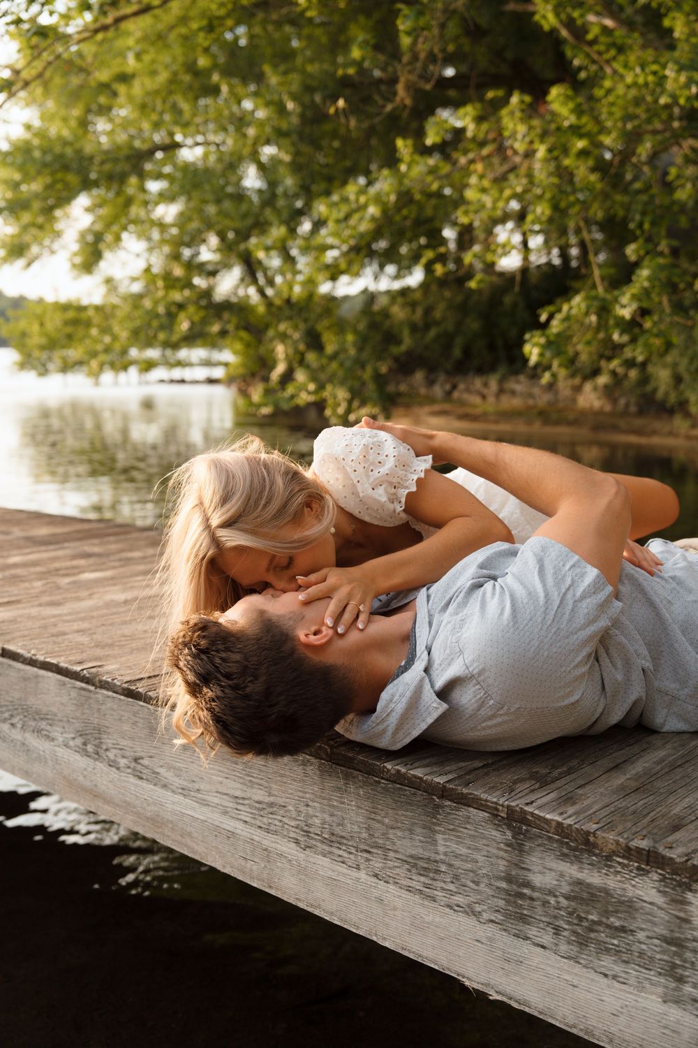 Two people sharing an intimate moment while lying on a wooden dock by the water.