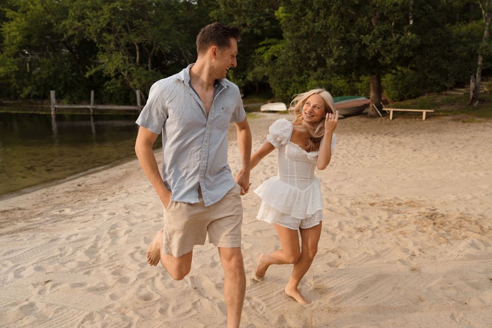 Two people running and laughing together on a sandy beach during golden hour.